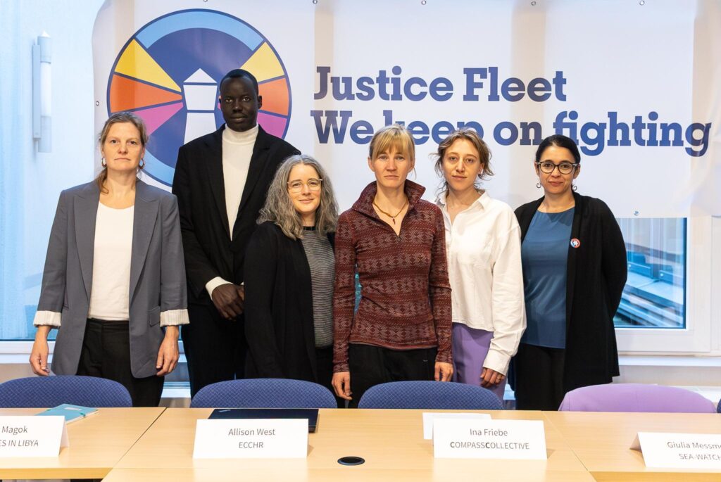 Sechs Leute schauen in die Kamera. Sie stehen vor einem Banner mit dem Logo der Justice Fleet und dem Spruch 'Justice Fleet - We keep on fighting'