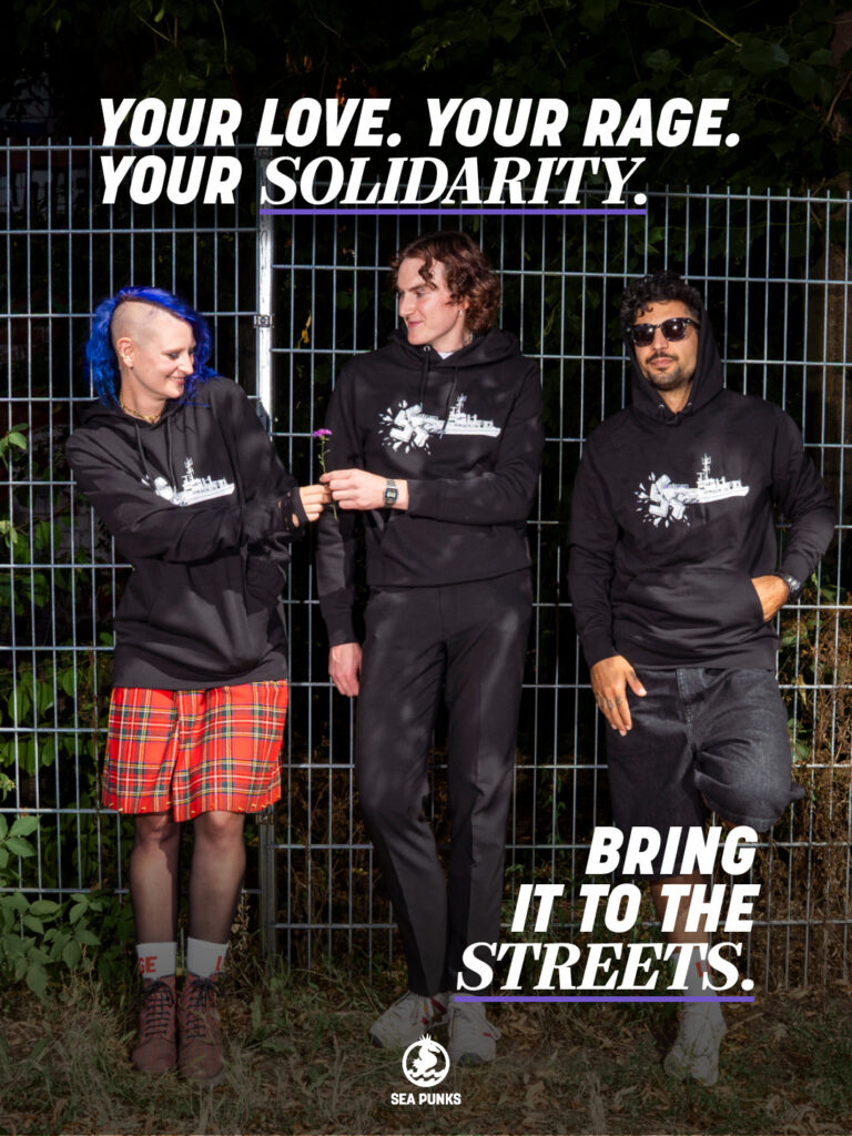 Drei Menschen in Sea Punks Hoodies vor einem Zaun
