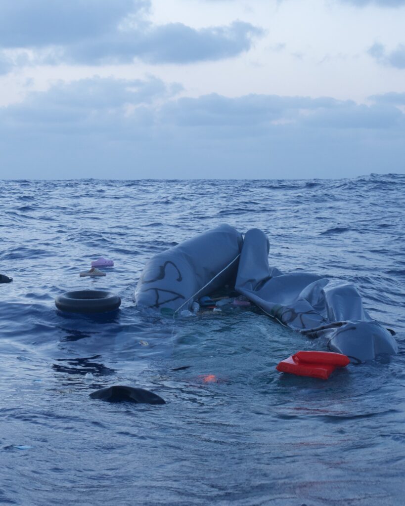 Wrecked rubber boat drifting at sea next to a life jacket