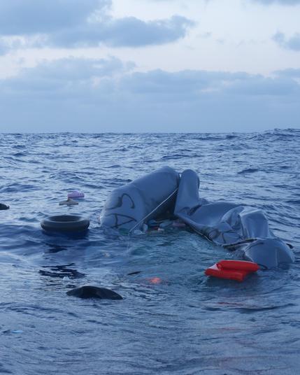 grey unseaworthy rubber boat sinking in the Mediterranean, shoes of survivors drowning